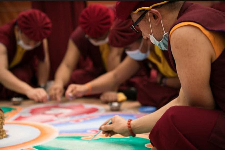 Hai vị tăng sĩ đang miệt mài kiến lập một Mandala cát, với các chi tiết phức tạp và màu sắc rực rỡ tượng trưng cho vũ trụ và giáo lý.