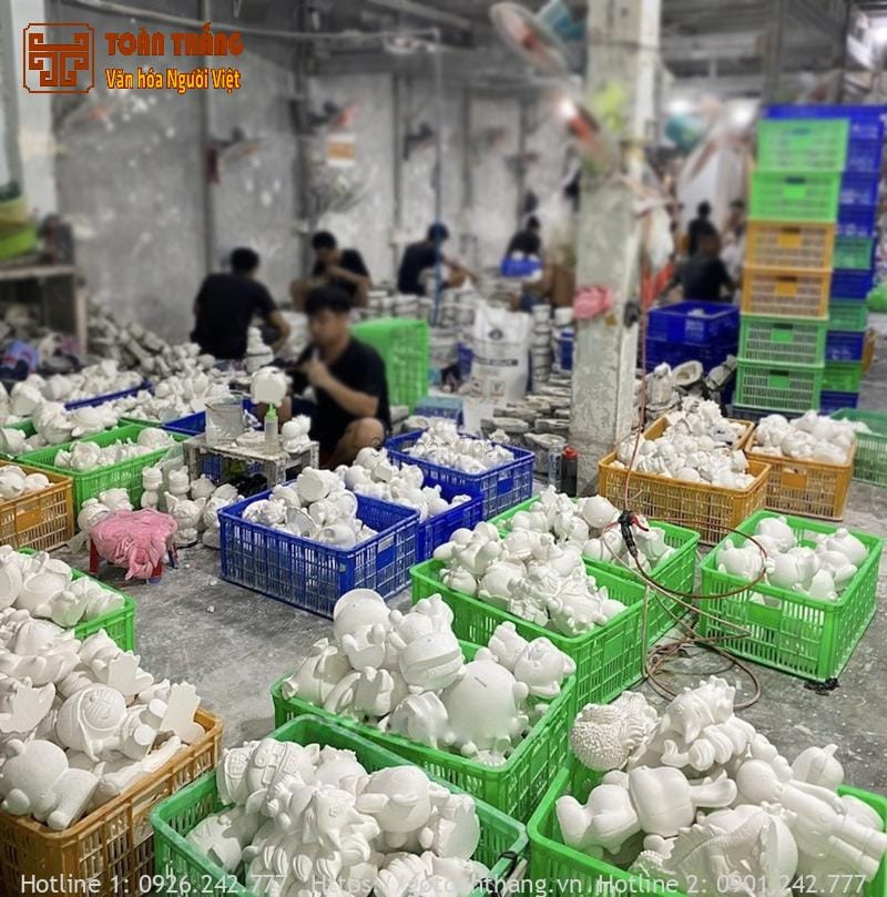 Một người trẻ đang cẩn thận tô màu cho tượng Thần Tài với bảng màu và cọ vẽ
