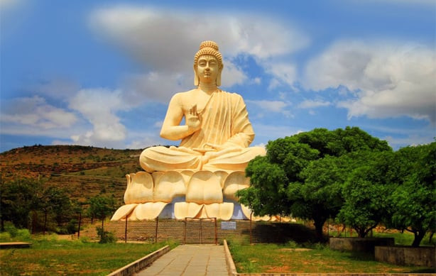 Người phụ nữ mặc pháp phục màu nâu đang ngồi thiền định hoặc cầu nguyện trong tư thế kiết già, hai tay chắp lại trước ngực.